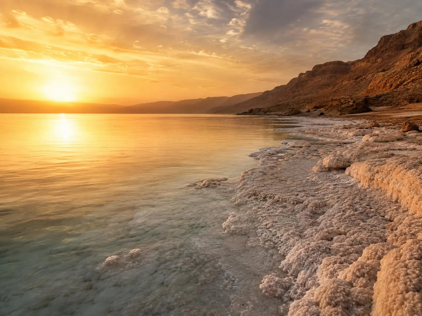 Sunrise over the Dead Sea with mineral salt formations along the shoreline